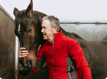 Man in red jacket hugging a horse.